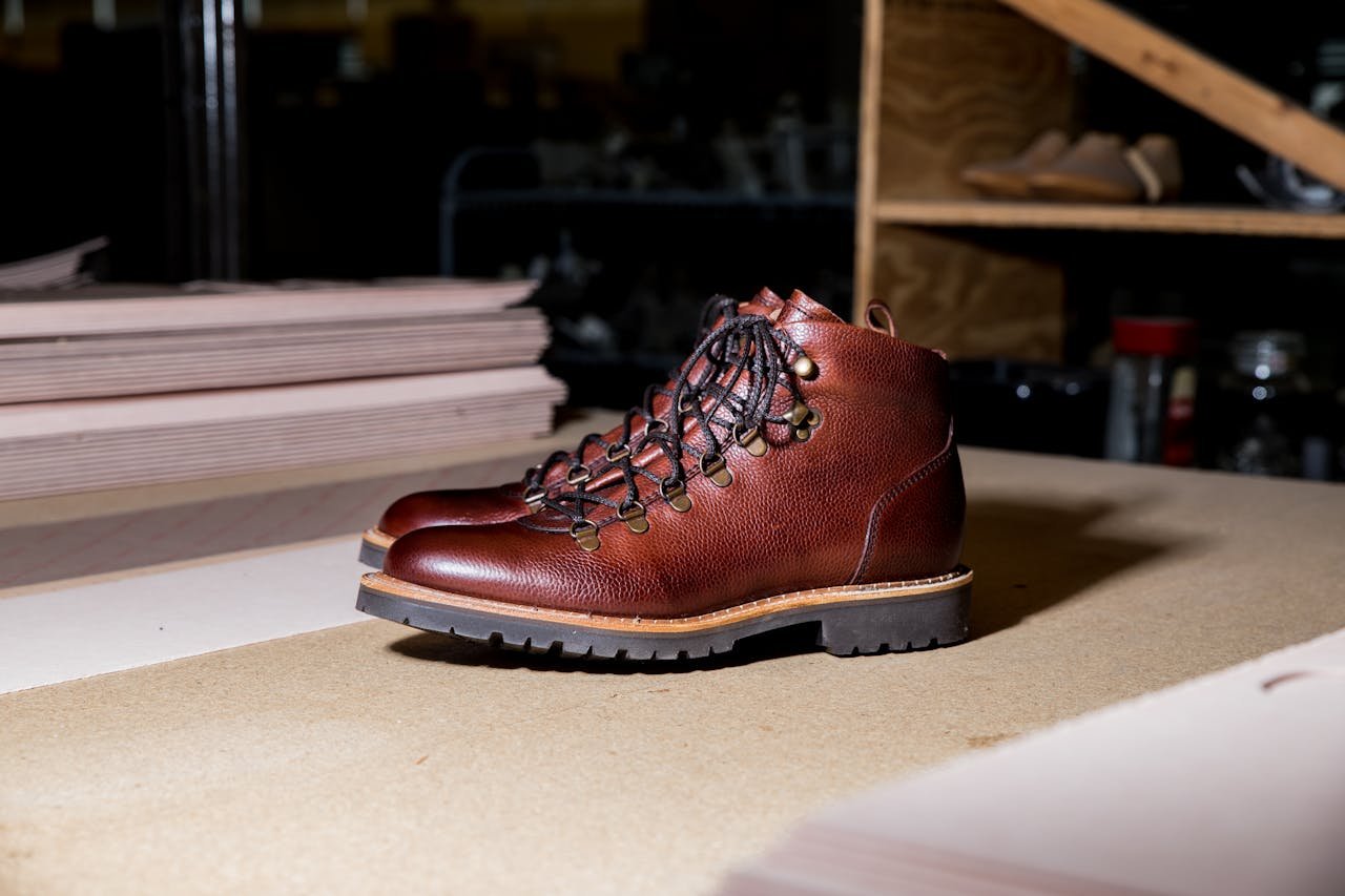 category-03 Close-up of brown leather boots with a rugged sole on a workshop table, showcasing craftsmanship.