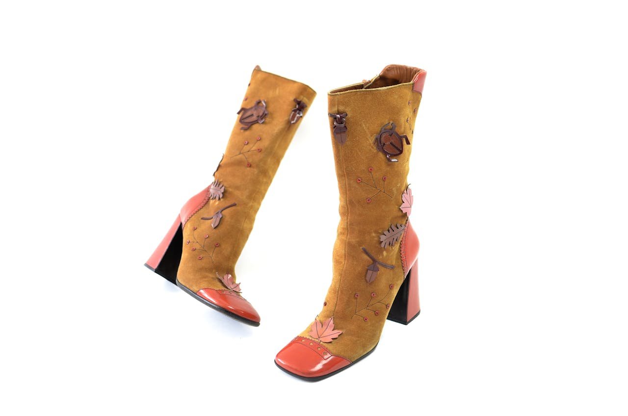 category-04 Pair of vintage suede brown boots with leather heels and nose decorated with tree leaves and bugs placed on white surface